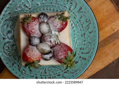 Top View. Delicious Sweet Cake With Strawberries And Grapes. A Piece Of Square-shaped Biscuit Cake In A Rounded Blue Plate On A Wooden Board. Sweet Life And Festive Mood Concept. Holiday. Food Photo