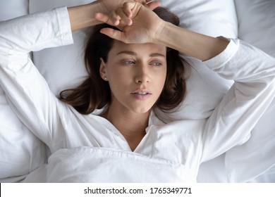 Top view of depressed sad young woman lie relax in bed look in distance thinking remembering, upset stressed millennial female rest in home bedroom feel sick suffer from illness or depression - Powered by Shutterstock