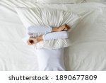 Top view depressed woman covering face with pillow, lying on bed at home alone, frustrated unhappy young female suffering from insomnia, mental or relationship problems, break up or divorce