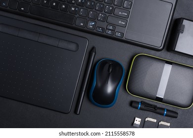 Top View Of Designer Work Place With Graphics Tablet, Memory Card, Keyboard, Portable Hard Drive On Black Background