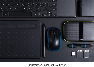 Top View Of Designer Work Place With Graphics Tablet, Memory Card, Keyboard, Portable Hard Drive On Black Background