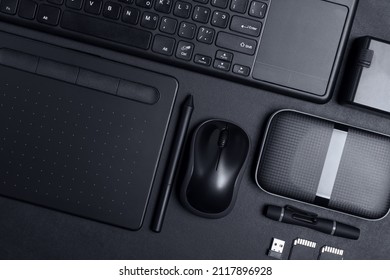 Top View Of Designer Work Place With Graphics Tablet, Memory Card, Keyboard, Portable Hard Drive On Black Background