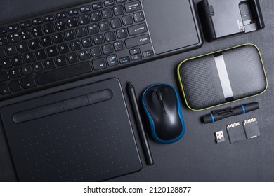 Top View Of Designer Work Place With Graphics Tablet, Memory Card, Keyboard, Portable Hard Drive On Black Background