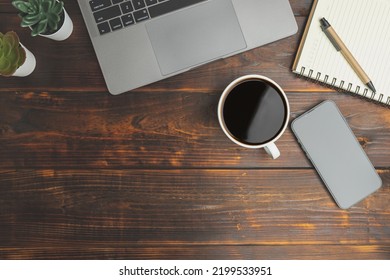 Top View Desk Of Work Office With Laptop, Smartphones, A Pen, Green Leaf, And Coffee Of Cup On Old Wooden Background With Copy Space. Flat Lay, Top View. Old Wood Office Table. 