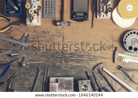 Top view of different goldsmiths tools on the jewelry workplace. Desktop for craft jewelry making with professional tools. Aerial view of tools over rustic wooden background. Poster design.