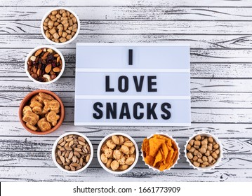 Top view of different kind of snacks as nuts, crackers and coockies in bowls on white wooden background horizontal