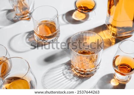 Top view of different shape glasses and bottle with whiskey with shadow on white table. Alcohol concept