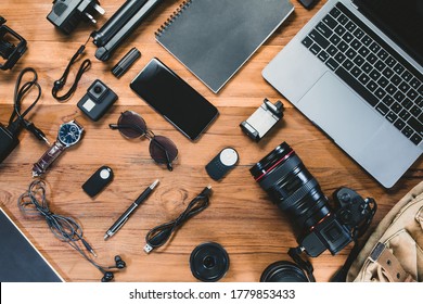Top view with a digital camera, charger, camera, lens, video camera, USB, personal laptop, book, pen, glasses, remote control, and electronics camera accessory photography concept on wooden background - Shutterstock ID 1779853433