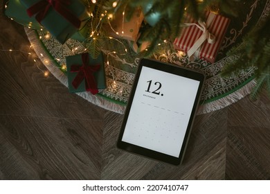 Top view of digital tablet with December calendar on screen laying with presents under Christmas tree. Holiday planning, online shopping, mockup. - Powered by Shutterstock