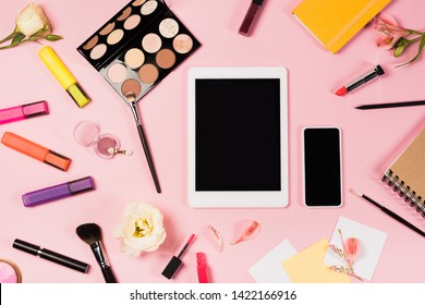 top view of digital tablet and smartphone with blank screen, notebooks, flowers and decorative cosmetics on pink - Powered by Shutterstock