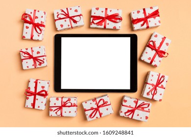 Top view of digital tablet surrounded with gift boxes on colorful background. Saint Valentine's day.