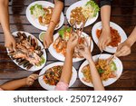 Top view of the dining table. Hands scooping food including grilled river prawns, seafood, fried chicken tendons, stir-fried chili paste, and fried soft-shell crab with garlic.