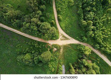 Top view of the dirt road with a crossroads and dense green forests. Beautiful bright landscape photography with drone on a summer day - Powered by Shutterstock