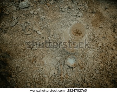 Top view of a dirty empty bottle and cap lying on dry rocky soil, soft natural lighting, highlighting environmental pollution and abandoned waste on arid ground