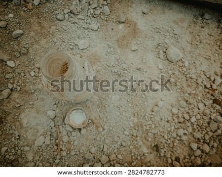 Top view of a dirty empty bottle and cap lying on dry rocky soil, soft natural lighting, highlighting environmental pollution and abandoned waste on arid ground