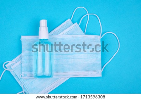Top view of disposable medical surgical protective face mask with antibacterial antiseptic spray for hands sanitizer on blue background. Protection against virus, flu or coronavirus. Square frame