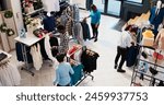 Top view of diverse customers checking stylish clothes, shopping for fashionable merchandise and accessories in modern boutique. Clients analyzing hangers with new fashion collection