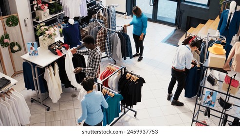 Top view of diverse customers checking stylish clothes, shopping for fashionable merchandise and accessories in modern boutique. Clients analyzing hangers with new fashion collection - Powered by Shutterstock