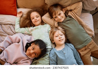 Top view at diverse group of children lying on bed together and looking at camera - Shutterstock ID 2307437025