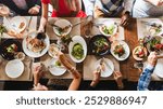 Top view of diverse group dining together, sharing food, enjoying a meal. Plates of food, hands reaching, diverse gathering, communal dining experience. Diverse people having dinner at restaurant.