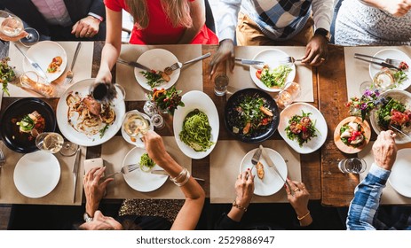 Top view of diverse group dining together, sharing food, enjoying a meal. Plates of food, hands reaching, diverse gathering, communal dining experience. Diverse people having dinner at restaurant. - Powered by Shutterstock