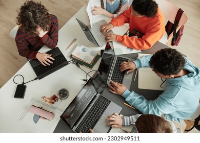 Top view at diverse group of teen school children using computers in classroom studying together at table - Powered by Shutterstock