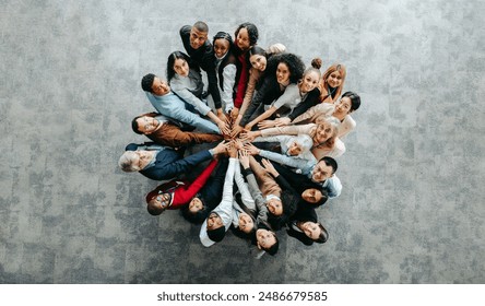 Top view of a diverse team of people joining hands in a collaborative and inclusive business environment, symbolizing unity and teamwork. - Powered by Shutterstock