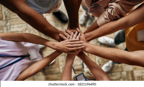 Top view of diverse young volunteers putting their hands on top of each other like a real team while standing in charitable organization office, Selective focus on hands, Web Banner - Powered by Shutterstock