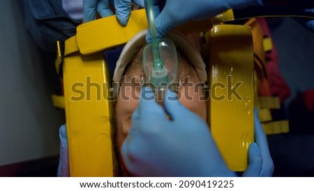 Top view doctors hands saving life of patient in ambulance car. Closeup professional paramedics fixing man head in immobilizer. Health care professionals in gloves putting oxygen mask on victim face 