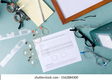 Top View Of Doctors Of Optometry Workplace. Eyeglasses, Blank Prescription, Professional Tools For Checking Eyesight, Documents On The Blue Table