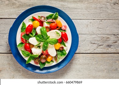 Top view of double plated fresh farm style caprese salad on a weathered wooden board
