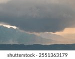 Top view of dramatic thick clouds over the hills in the afternoon. Black clouds and orange sky light. Background view of the hills