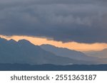 Top view of dramatic thick clouds over the hills in the afternoon. Black clouds and orange sky light. Background view of the hills
