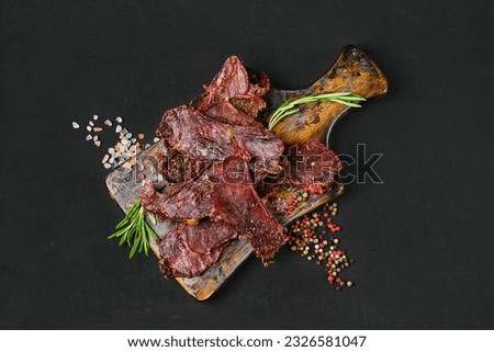 Top view of dried beef jerky slices on wooden board with salt and pepper