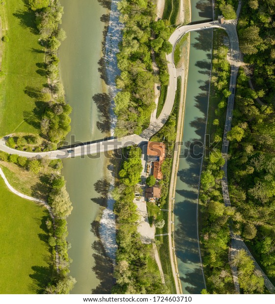 Top view from a drone at a\
driving car at a bridge over a river with a neaby forest and a\
house