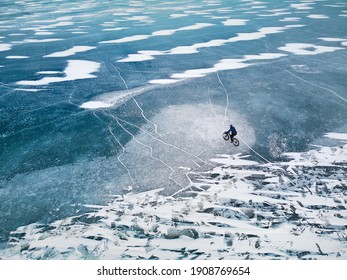 Top view drone shoot of man at bicycle riding on the frozen lake with ice texture.
