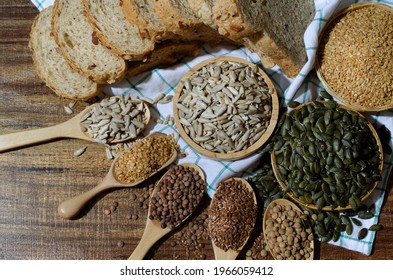Top view of dry organic sunflower seeds in wooden bowl over blur wholewheat bread, golden flax and pumpkin seed on white table cloth in dark brown tone 