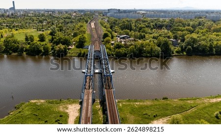 Top view of dual railway bridge tracks extending across a river in lush Polish landscape with dense forest and city in background