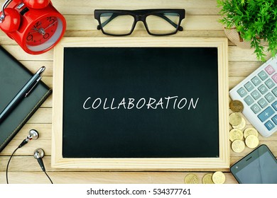 Top View Of Earphone, Notebook, Pen, Alarm Clock, Spectacle, Small Green Tree, Calculator, Coins, Smartphone And Black Chalkboard Written With COLLABORATION Inscription On Wooden Table.