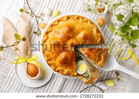 Top view of Easter table, with colored eggs, flowers, Savory Easter pie, Torta Pasqualina, made with spinach, silverbeet, leek, cheese and whole boiled eggs, originated in Italy.  Homemade food.