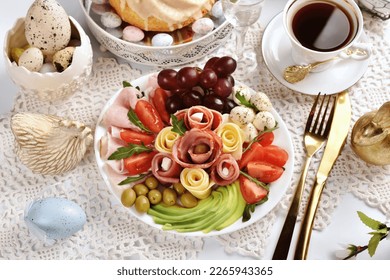 Top view of Easter table with a platter with sliced ham, salami, cheese, avocado, mozzarella and tomatoes and decorations