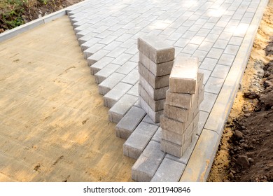 Top view of the edge of surface with laid gray paving slabs. Surface with sandy mixture is visible. Two stack of paving slabs is ready for laying.