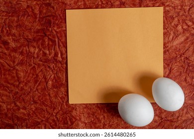 Top view of eggs and blank note on vibrant red fabric background.