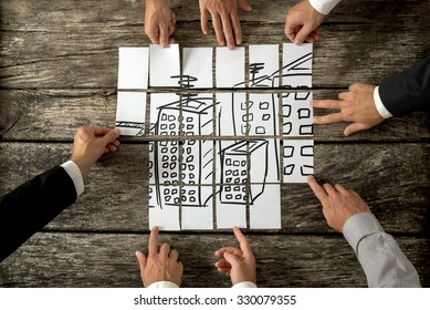 Top View Of Eight Architects Or Urban Planners Cooperating In Urban Development And Use Of Land By Assembling Hand Drawn Image Of High Buildings On White Cards. 