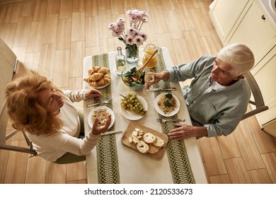 Top View Of Elderly Caucasian Couple Drinking Wine While Having Dinner At Home. Family Relationship And Enjoying Time Together. Domestic Lifestyle. Idea Of Romantic Date. Man And Woman Sit At Table