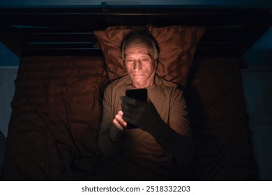 Top view elderly man using mobile phone laying on the bed at night in bedroom. Sleepy exhausted senior male, can not sleep. Insomnia and mobile addiction concept. - Powered by Shutterstock