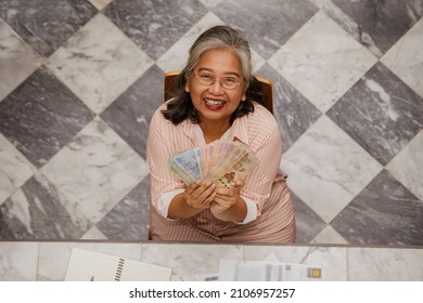 Top View Elderly Woman Sitting Excitedly Enjoying The Old Age Pension, Holding Cash, Celebrating Wealth At Home : Health Care, Joyful Quality Of Life, Freedom, Relaxation, Retirement Concept.