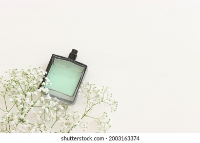 Top view of elegant perfume bottle with flowers over wooden white background. Cosmetics, fragrance and perfumery concept