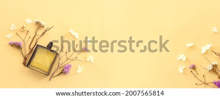 Top view of elegant perfume bottle with flowers and oud over yellow background. Cosmetics, fragrance and perfumery concept