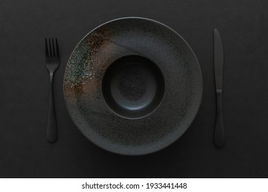 Top view  of empty black ceramic plate for pasta, with an abstract pattern and black cutlery on a black background. Flat lay. Minimal design concept